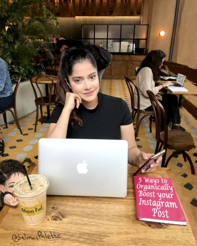 a girl in a coffee shop with brown hair in a pony tail with a laptop and iced coffee open.